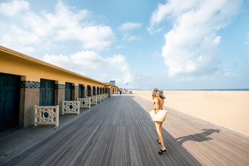 Woman walking on the beach with locker rooms in Deauville, famous french resort in Normandy. Wide angle view - obrazy, fototapety, plakaty