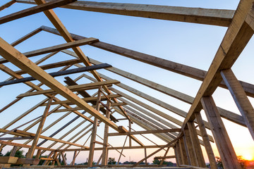 New wooden house under construction. Close-up of attic roof frame against clear sky from inside....