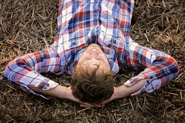 Young Man in Flannel Shirt Relaxing on Hay Bale on Autumn Day