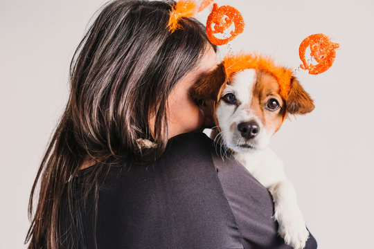 young woman holding her cute small dog over white background. Matching pumpkin diadems. Halloween concept. Indoors