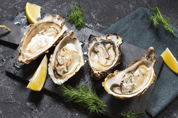 Opened Oysters with lemon on dark stone background