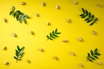 Pistachios with leaves on yellow background, flat lay. Pattern of pistachio nuts and leaves. Top view