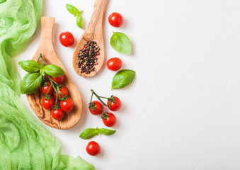 Organic Cherry Sugardrop Tomatoes on the Vine with basil in oilve wood plate and spoon with pepper on white kitchen background. Space for text