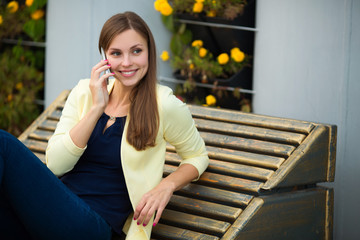 beautiful young girl in a yellow jacket talking on the phone in the park in summer