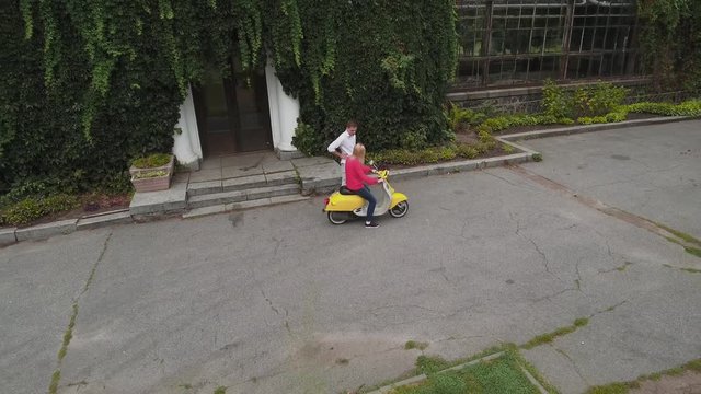 Girl is sitting on a scooter near the park house. Shot on drone