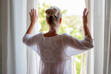 Newly lifted woman looking out the window in pijama