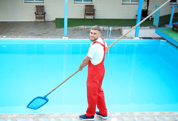 Male worker cleaning outdoor pool with scoop net