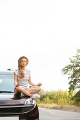 Young woman meditating on car hood outdoors. Joy in moment
