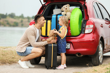 Father and daughter near car trunk with suitcases on riverside