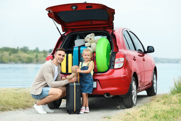 Father and daughter near car trunk with suitcases on riverside