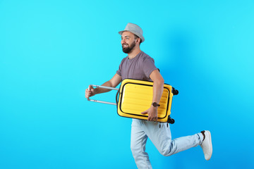 Man with suitcase running on color background. Vacation travel