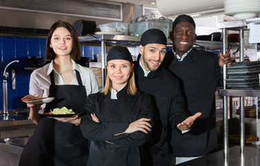 Woman waiter with command of cooks are posing together on kitchen in restaurant.