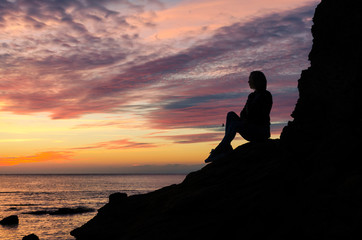 The silhouette of girl that standing on the stone near the sea