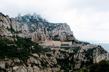 Naklejka premium Montserrat, Catalonia, Spain. Top View Of Hillside Cave Santa Cova De Montserrat Or Holy Cave Of Montserrat In Summer Day. Santa Maria De Montserrat Abbey.