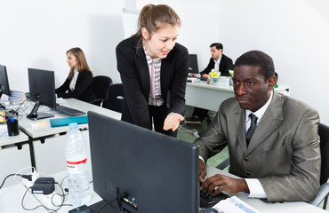 Attractive girl helping African American male colleague in work in modern coworking space