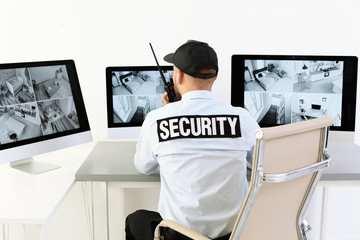 Male security guard with portable transmitter monitoring home cameras indoors