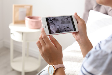 Woman monitoring modern cctv cameras on smartphone indoors, closeup