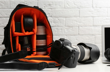 Naklejka premium Camera and backpack with professional photographer's equipment on table indoors