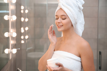 Beautiful woman with clean towels applying face cream in bathroom