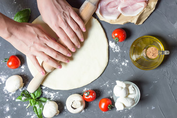 hands rolling out pizza dough, raw pizza ingredients, rolling pin, dough basis