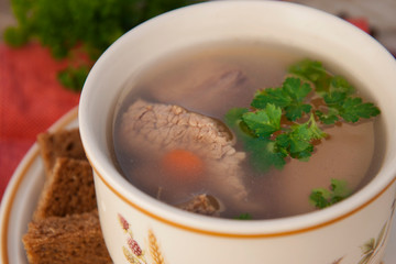 Clear beef broth, bouillon in white bowl and vegetables on wooden table. Rustic style.