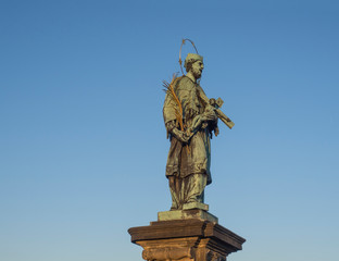 Obraz premium Baroque Statue of Saint John of Nepomuk with Golden Star Halo holding crucifix with Jesus Christ on Charles Bridge in Prague, Czech Republic, sunny day, clear blue sky