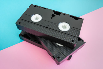 Stack of 3 black VHS cassettes on a pink and blue background.