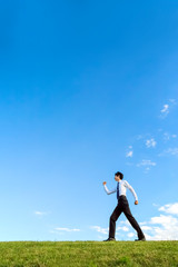 青空をバックにYシャツ姿で前進する若いビジネスマン1人。元気・成功・目標・挑戦イメージ