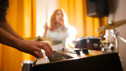 Repetition. Girl drummer and a guy on keyboards. Focus from hands to drums. Backlight