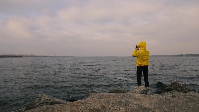 Hiking traveler man in yellow jacket walking alone at river, take a picture by smartphone