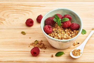 Homemade granola in a bowl with raspberries on a wooden table.