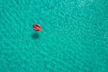 Aerial view of slim woman swimming on the swim ring  donut in the transparent turquoise sea in Seychelles. Summer seascape with girl, beautiful waves, colorful water. Top view from drone