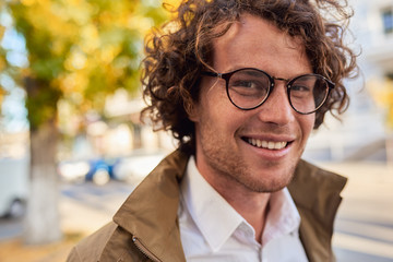 Closeup horizontal portrait of young happy business man with glasses smiling and posing outdoors....