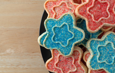 Top close view of several star shaped sugar cookies with blue and red sprinkles on a black dish atop a wood table top.
