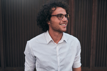 Urban shot of handsome young businessman with glasses, smiling, posing outdoors. Male student...