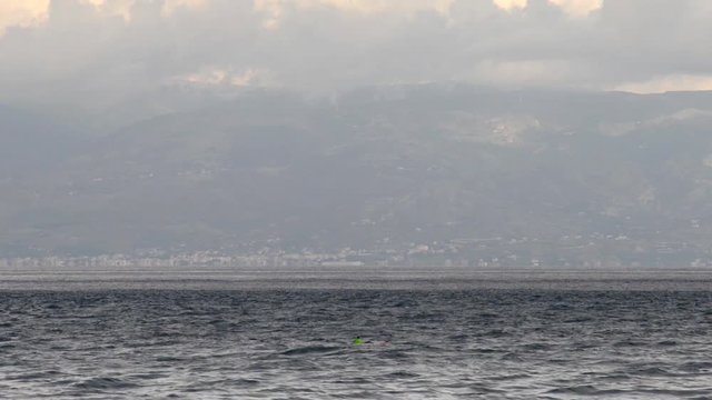 Una piccola barca mossa dalle onde e dalla corrente dello Stretto di Messina e sullo sfondo la Calabria