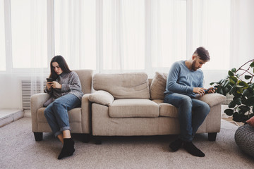 Couple in living room using smart phones. Young people chatting online.