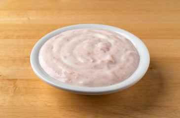 A bowl of strawberry rhubarb yogurt sweetened with honey on a wood table.