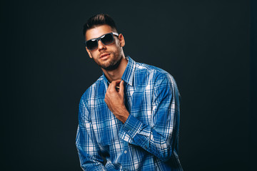 Fototapeta premium Handsome man with sunglasses posing in studio on dark background