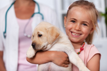 Happy little girl holding her cute puppy dog at the veterinary doctor office
