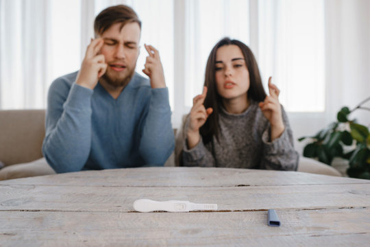 Hopeful Couple Checking A Pregnancy Test. Man And Woman Cross Fingers Waiting For Test Results