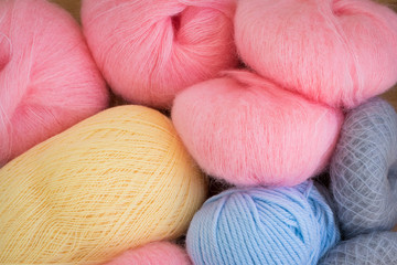 Colorful balls of yarn lying on a beige wooden background taking up the whole frame