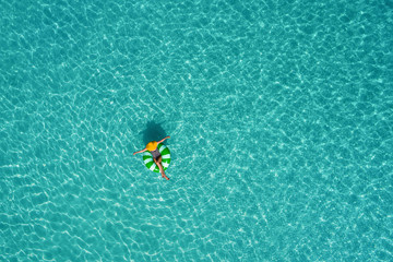 Aerial view of slim woman swimming on the swim ring  donut in the transparent turquoise sea in Seychelles. Summer seascape with girl, beautiful waves, colorful water. Top view from drone