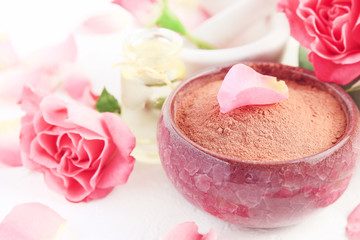 Pink clay powder in bowl for making face mask, holistic beauty treatment and skin care, fresh rose petals essential oil. Close up with soft light. Delicate skin cleanser