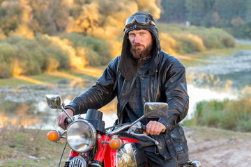 Biker in a leather jacket and helmet on a retro motorcycle in the forest