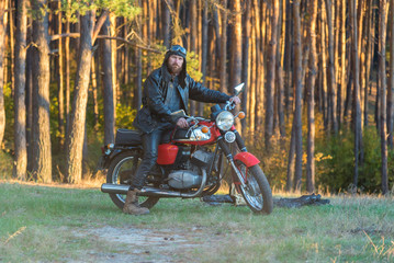 Biker in a leather jacket and helmet on a retro motorcycle in the forest