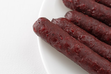 Close view of several barbecue flavor small smoked pork sausages on a plate atop a white tablecloth.