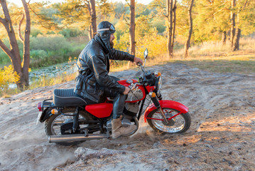 Biker in a leather jacket and helmet on a retro motorcycle in the forest
