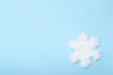 White snowflake made of artificial snow on a blue background. Winter backdrop, frost. Top view, copy space, flat lay