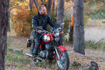 Fototapeta na wymiar Biker in a leather jacket and helmet on a retro motorcycle in the forest